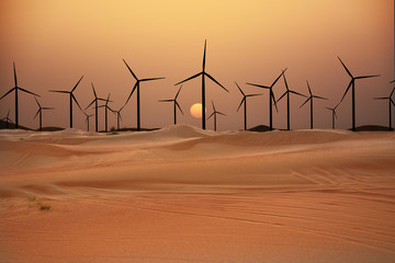 Wind turbines in the desert suggesting renewable energy concept with sand dunes at sunset - 296613323