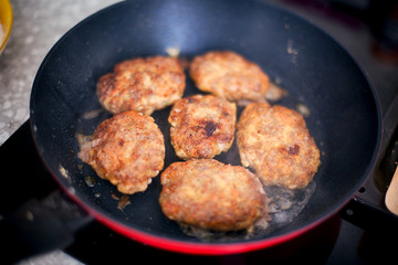 Homemade cutlets in frying pan cooking on induction hob in domestic kitchen.