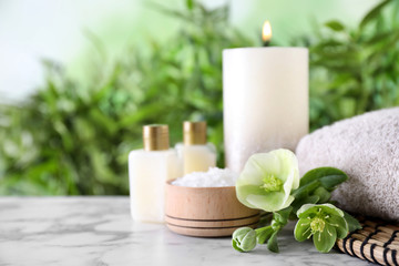 Composition with flowers, sea salt and towel on white marble table against blurred background, space for text. Spa concept