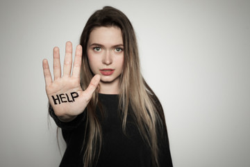 Young woman with word HELP written on her palm against light background, focus on hand. Space for...