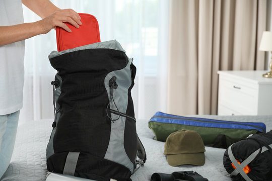 Woman packing different camping equipment into backpack at home, closeup