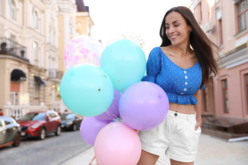Fototapeta na wymiar Beautiful young woman with color balloons on city street