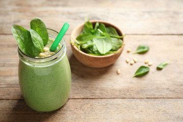 Jar of healthy green smoothie with fresh spinach on wooden table. Space for text