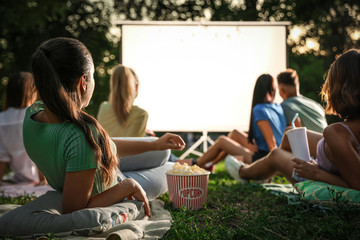 Young people with popcorn watching movie in open air cinema. Space for text - obrazy, fototapety, plakaty