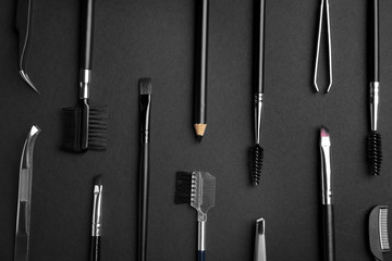 Set of professional eyebrow tools on black background, flat lay