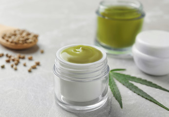 Fototapeta na wymiar Jars of hemp cream and seeds on grey table. Organic cosmetics