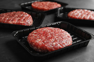 Plastic containers with raw meat cutlets for burger on grey table, closeup