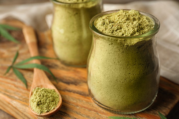 Jars of hemp protein powder on wooden board, closeup. Space for text