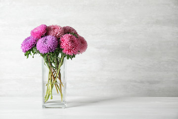 Glass vase with beautiful aster flowers on table against light background. Space for text