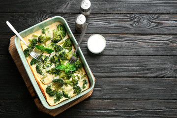 Tasty broccoli casserole in baking dish on black wooden table, flat lay. Space for text