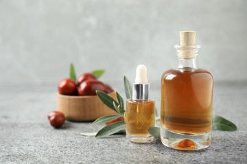 Glass bottles with jojoba oil on stone table against grey background. Space for text