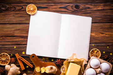 Traditional christmas holidays pastry ingredients, kitchen utensils and open blank notebook on wood textured table. Ginger cookies recipe concept. Close up, copy space, top view, flat lay, background.