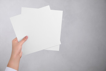 Young woman holding blank paper sheets on light grey background, closeup. Mock up for design