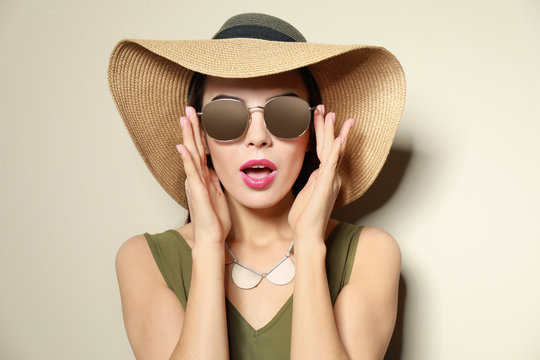 Emotional woman in stylish sunglasses and hat on beige background