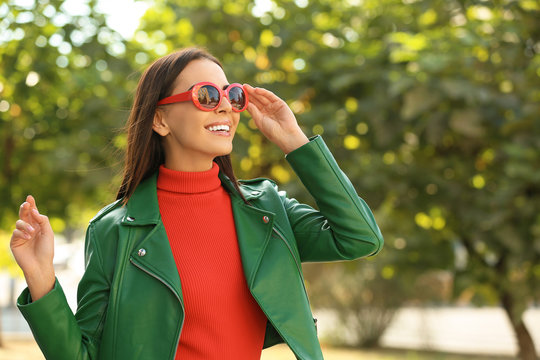 Beautiful woman wearing red sunglasses in green park