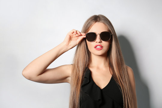 Young woman wearing stylish sunglasses on light background