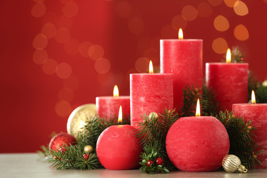 Burning candles and Christmas decor on table against red background with bokeh effect