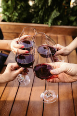People clinking glasses with wine on the summer terrace of cafe or restaurant. Happy cheerful friends celebrate summer or autumn fest. Close up shot of human hands, lifestyle.