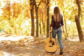 Teen girl with acoustic guitar in autumn park, back view