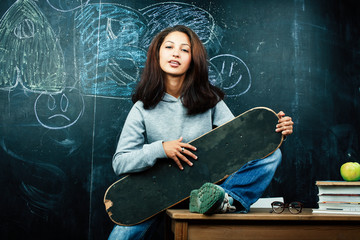 young cute teenage girl in classroom at blackboard seating on table smiling, modern hipster concept