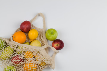 Mesh shopping bag with fruits apples, oranges, lemon and pears on white background.