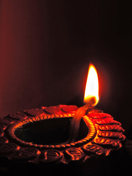 Close up isolated low key diwali oil clay lamp,chirag or panti on a dark orange black background with bright orange red light illuminating clay lamp