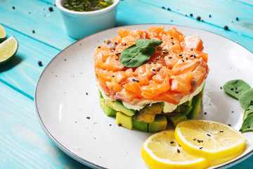 Delicious avocado and salted salmon tartar on wooden background.