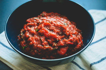 Sauce of baked bell pepper and eggplant with parsley. Red sauce. Dark blue bowl and napkin.