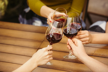 People clinking glasses with wine on the summer terrace of cafe or restaurant. Happy cheerful friends celebrate summer or autumn fest. Close up shot of human hands, lifestyle.