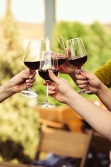People clinking glasses with wine on the summer terrace of cafe or restaurant. Happy cheerful...