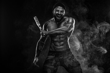 Fototapeta na wymiar Strong and fit man bodybuilder with baseball bat shows abdominal muscles under a t-shirt. Sporty muscular guy athlete. Sport and fitness concept. Men's fashion.
