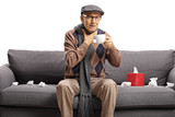 Elderly man with a sore throat sitting on a couch and drinking tea