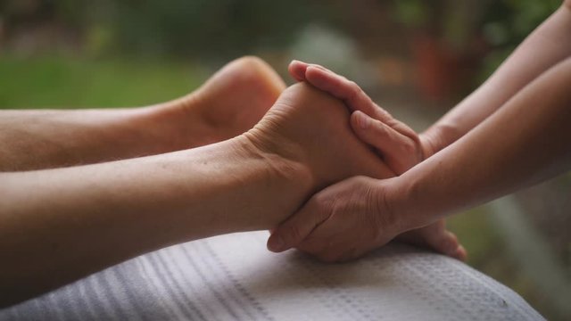 Close Up Shot showing, therapist touching feet during reiki treatment outdoor in the nature. Calm down an relax person.