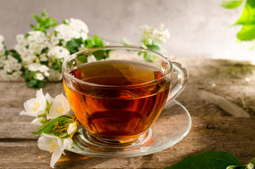 Tasty fragrant tea with jasmine flower. Glass tea cup on a old wooden table. Hot drink with philadelphus flowers.