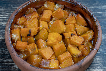 Baked yellow pumpkin with honey, olive oil and spices on a plate on the wooden table. Vegetarian food. Closeup