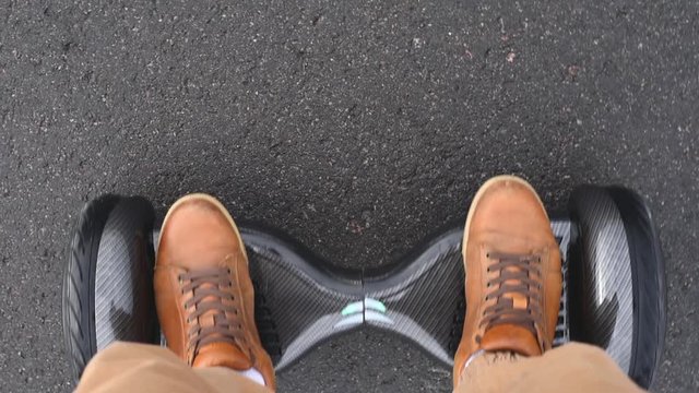 Man start moving on gyro scooter on asphalt road, top view. Closeup of man legs on self balance hoverboard outdoors
