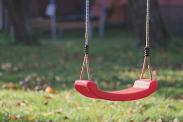 Empty red swing on children playground in the park in autumn season. Missing child. Lonely swing in sunny autumn day.