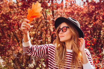 Portrait of a blonde in the autumn forest. Beautiful girl in a black hat walks in the park. Woman in stylish accessories outdoors. Portrait of a girl on the nature at sunset. red autumn background