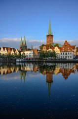 Obraz premium Cityscape of the historic old town of Luebeck in Germany with reflection in the river Trave, illuminated by the setting sun late afternoon, dark blue water and sky, copy space