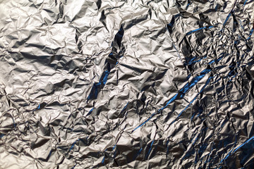 Background texture of crumpled aluminum leaf foil with blue highlights, closeup.