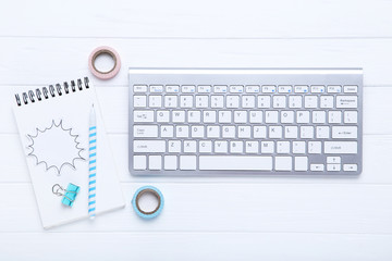 Computer keyboard with office supplies on white wooden table