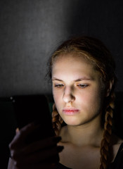 portrait of young teenager redhead girl with long hair with smartphone in dark room