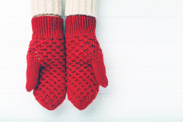 Hands in knitted mittens on white wooden table