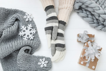 Hands in knitted mittens with hat, scarf and gift boxes on white wooden table