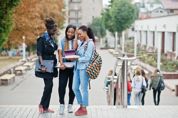 Three african students female posed with backpacks and school items on yard of university and look...