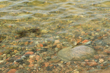 Multi-colored stones under the sea waves. In the foreground is a large stone, on which water flows. Texture for creative design.