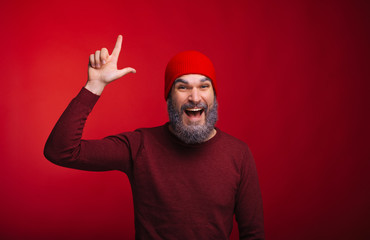 Naklejka premium Cheerful handsome bearded hispter man pointing at copyspace over red background