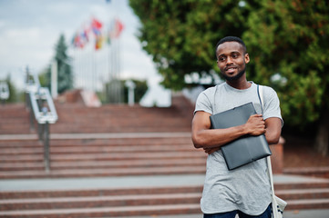 African student male posed with backpack and school items on yard of university, against flags of...