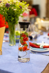 a carafe filled with water and strawberries stands on a served blue table.  close up, soft focus. served table is on background in blur