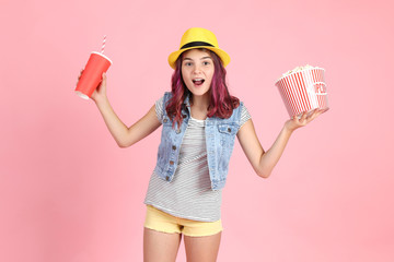 Young girl holding bucket with popcorn and paper cup on pink background